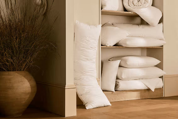Shelves with neatly arranged pillows and a decorative vase on a wooden floor.